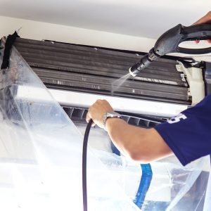 The technicians are cleaning the air conditioner by spraying water. Hand and water spray are cleaning the air conditioner on white background.