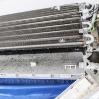 The technicians are cleaning the air conditioner by spraying water. Hand and water spray are cleaning the air conditioner on white background.